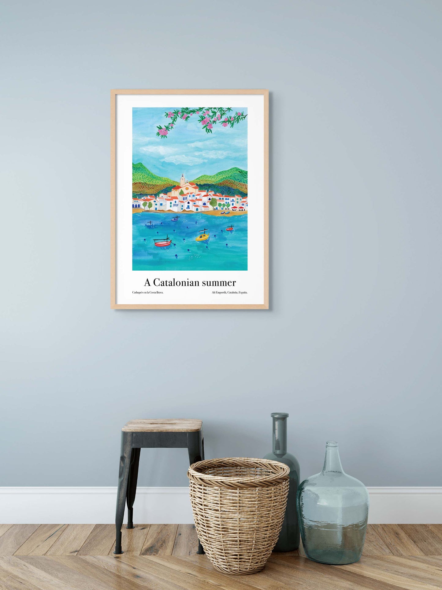 A room with an art poster on the wall of a travel illustration of the town on Cadaques on the Mediterranean coastline of Catalonia.