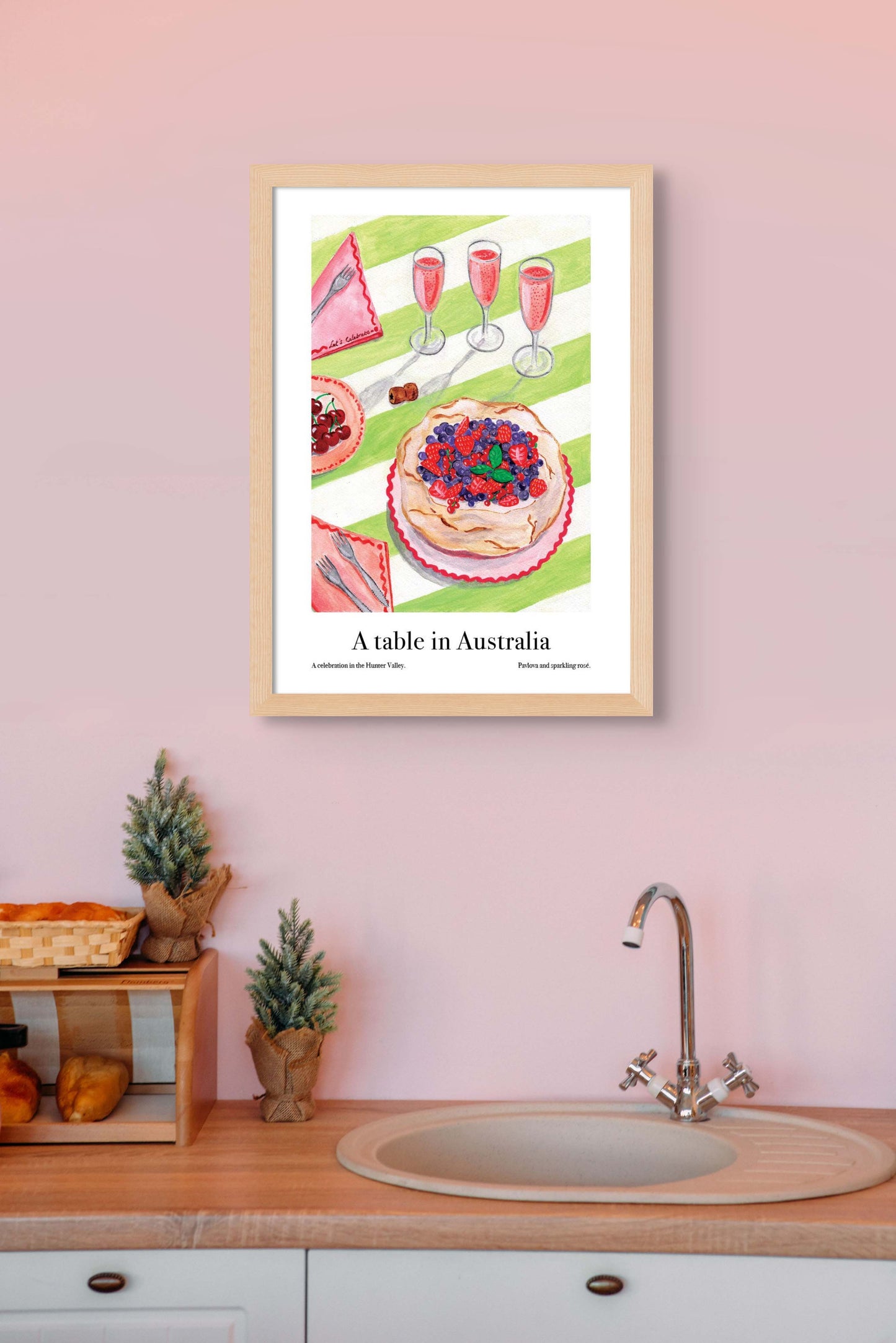 A kitchen with an art poster on the wall of a table in Australia, featuring pavlova and sparkling wine.