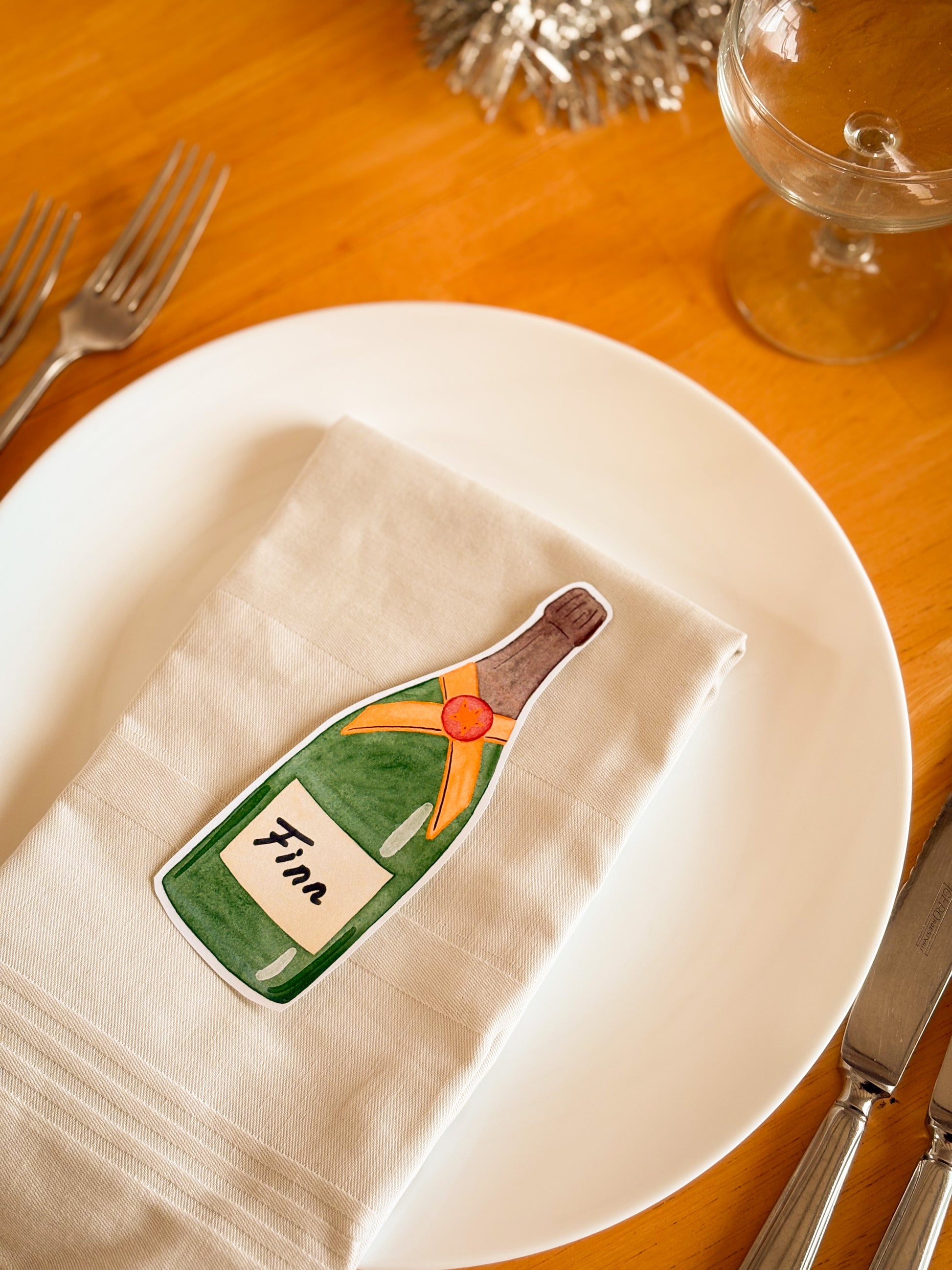 Napkin with a Champagne bottle Placement Card on a white plate with cutlery