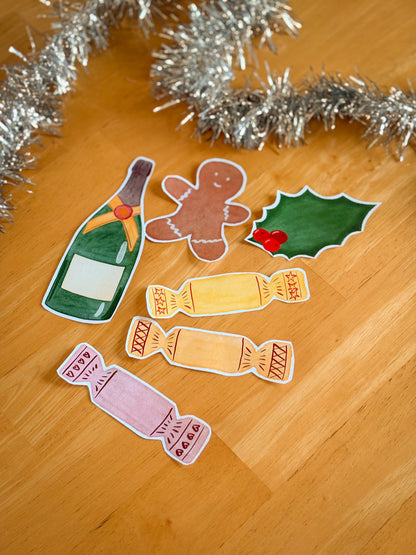 Decorative elements of a bottle, gingerbread man, holly, and candies on a wooden surface with tinsel.