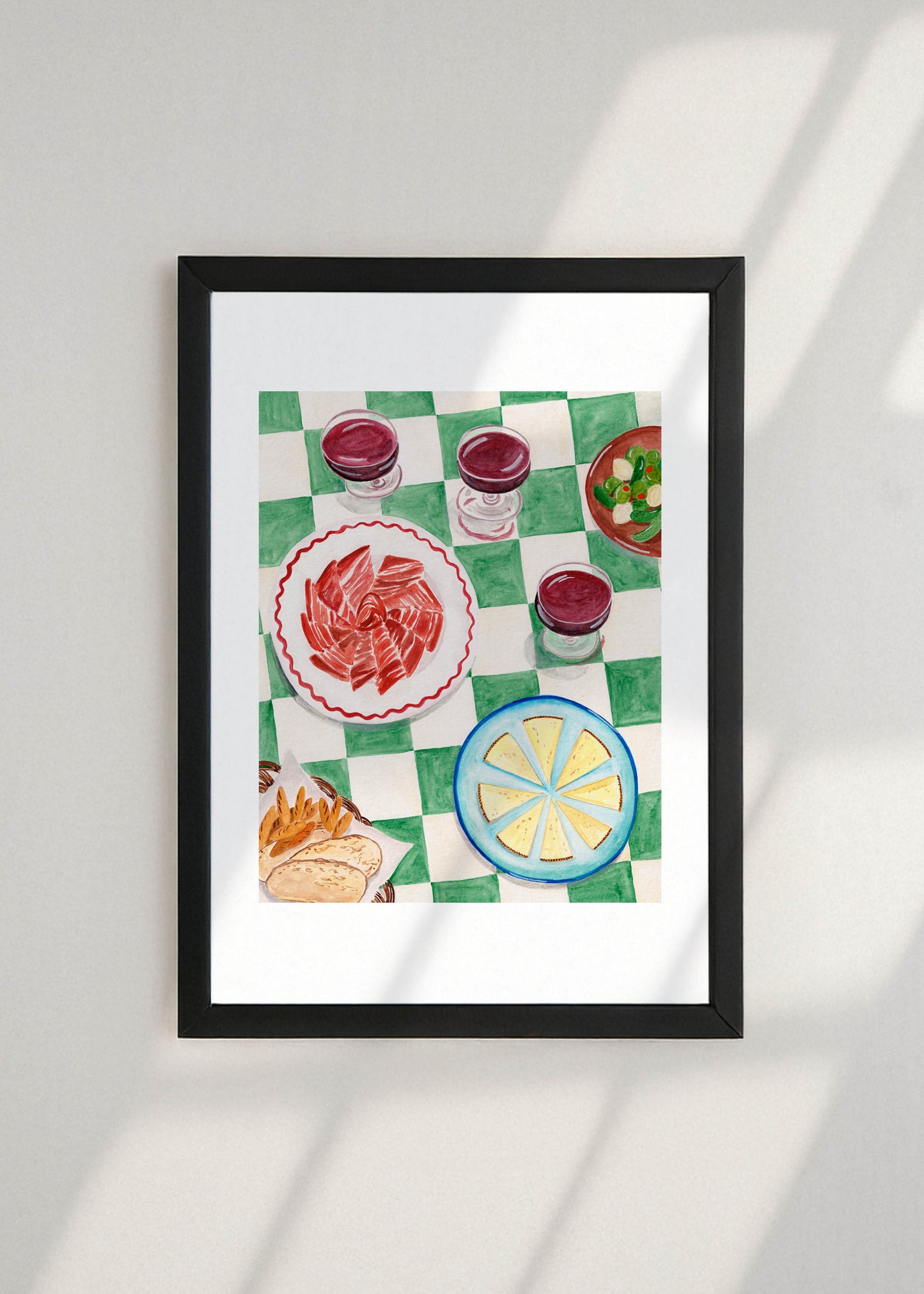 Framed artwork of a table with a checkered tablecloth, Spanish tapas and wine on a white wall.