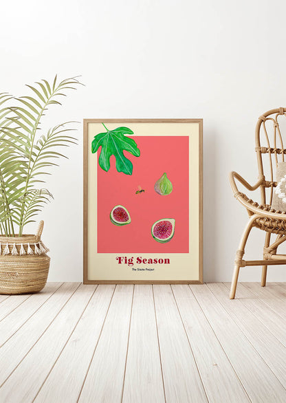 Framed artwork with fig illustrations on a pink background in a room with a plant and chair.