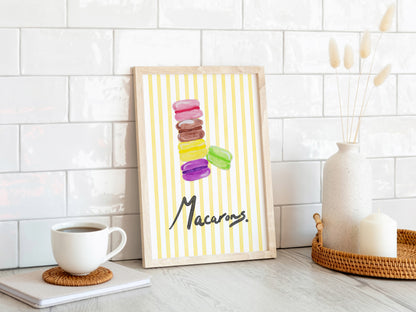 Framed artwork of colorful macarons on a white wall with a coffee cup and decor items.
