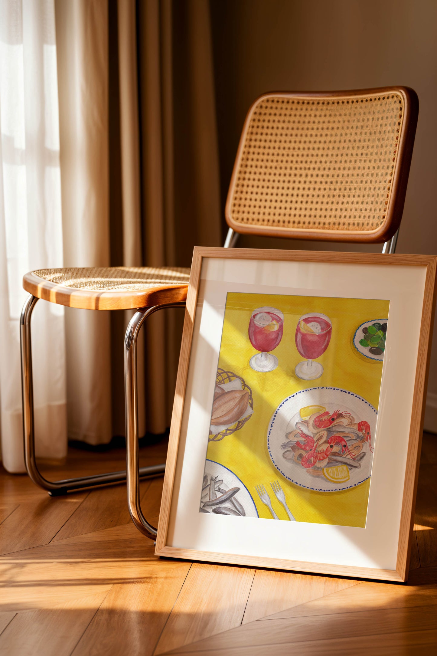 Framed artwork of a Spanish Food Art Print on a wooden floor with a wicker chair and stool in the background.
